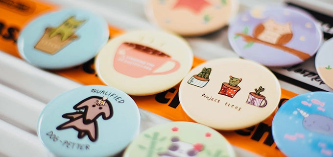 Individuelle Buttons liegen auf einem Tisch. Die bunt bedruckten Buttons eignen sich hervorragend als Werbegeschenk für Konzertbesucher.