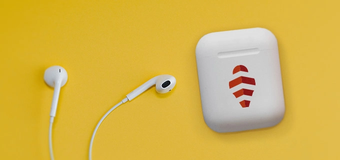Kopfhörer mit Logo liegen auf einem gelben Tisch. Daneben liegt ein weißes Case der bedruckten Kopfhörer, das mit einem roten Logo bedruckt ist. Ideal für Tech-Startups
