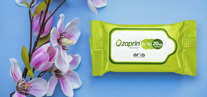 Erfrischungstücher mit Logo auf einer blauen Fläche. Die Verpackung ist grün und trägt ein gut sichtbares Logo. Daneben ist eine Blume zu sehen.