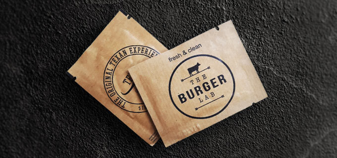 Erfrischungstücher mit Logo liegen auf einem edlen schwarzen Untergrund. Auf den Verpackungen der bedruckten Erfrischungstücher sind Kühe abgebildet.