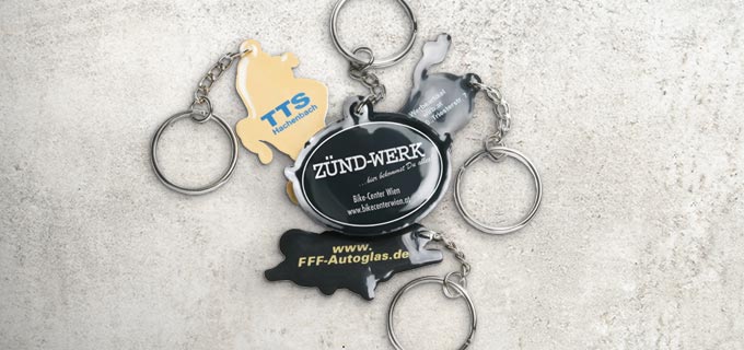 Bedruckte Schlüsselanhänger in Sonderform liegen zusammen auf einem Haufen. Die Schlüsselanhänger haben unterschiedliche Formen und unterscheiden sich in Design und Farbe.